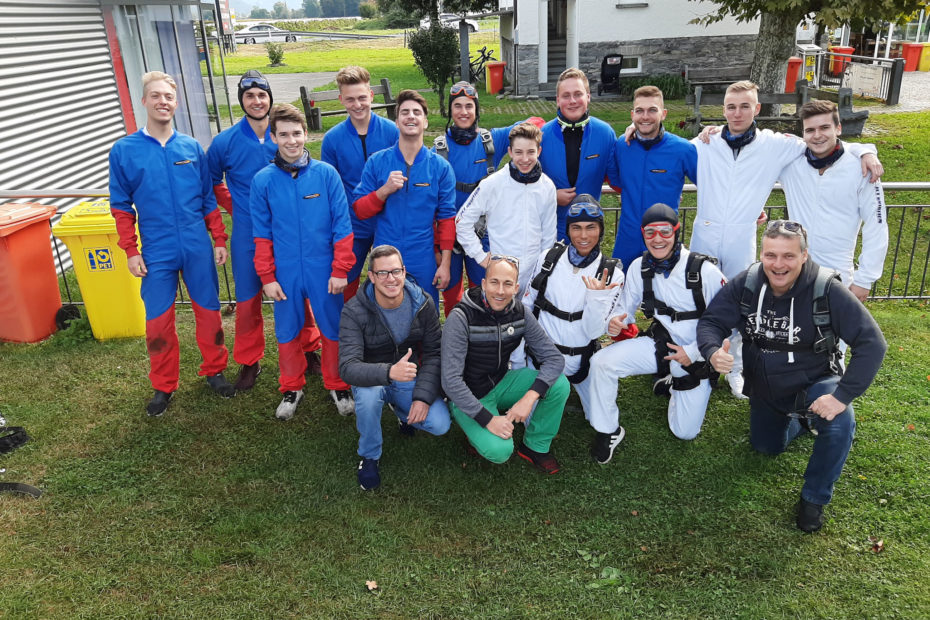Gruppenfoto vom Teamausflug zum Fallschirmspringen, alle im blauen Overall
